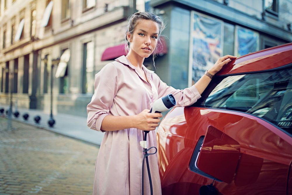 Portrait of young girl charging her electric car in the city